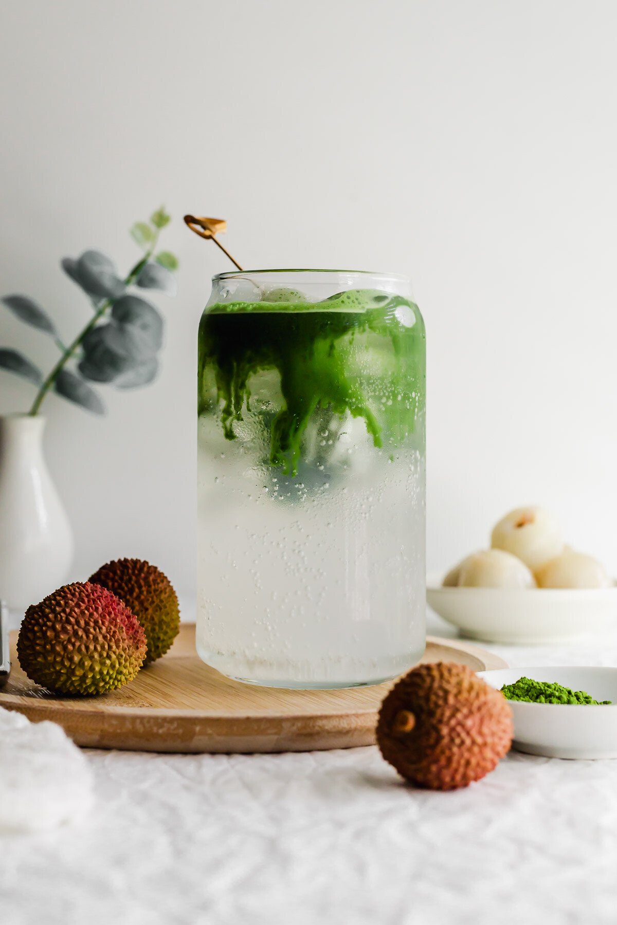 Matcha lychee soda in a glass on wooden plate.