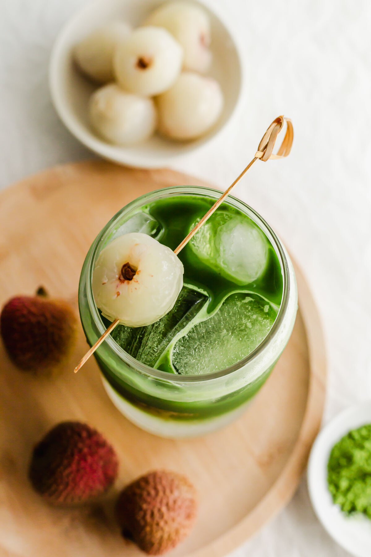Matcha lychee soda in a glass with a lychee skewer.