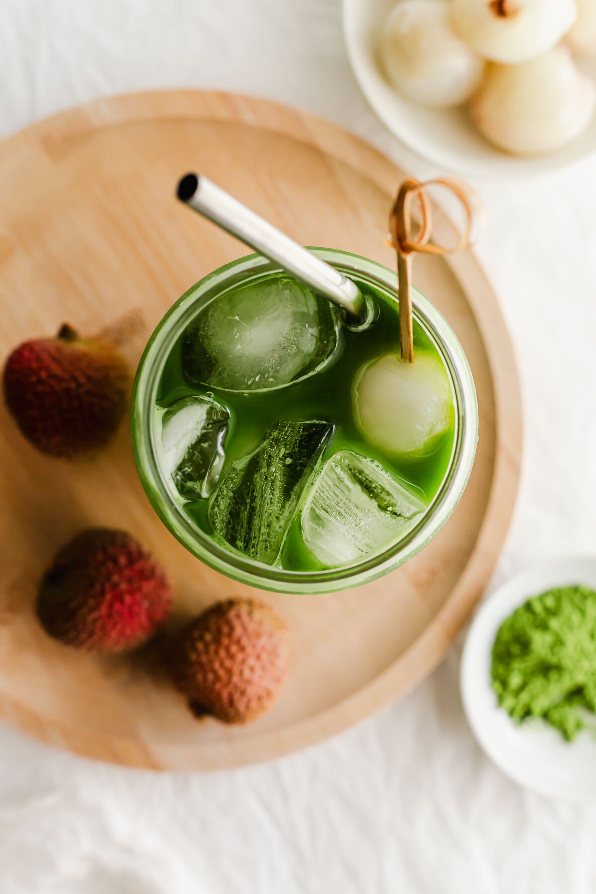 Matcha lychee soda in a glass with metal straw on wooden plate.