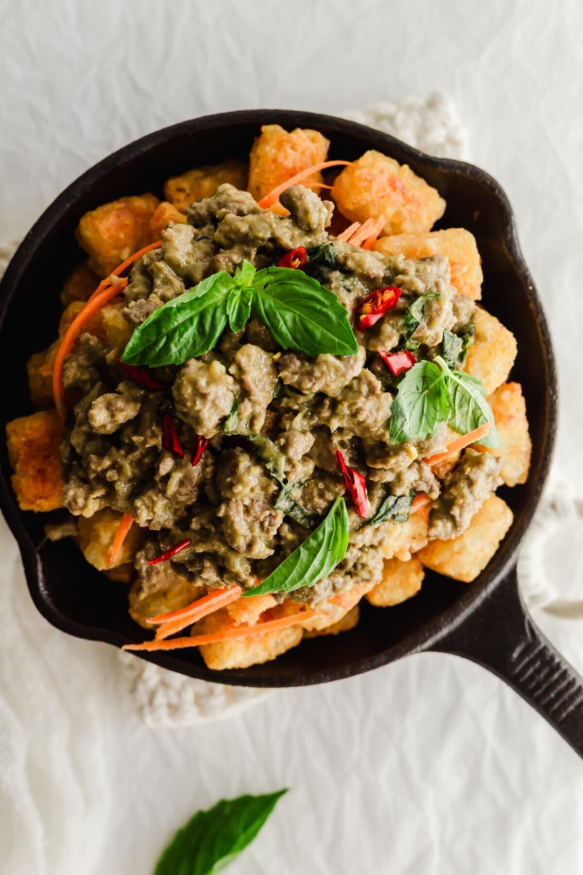 Thai green curry chicken on a bed of tater tots in skillet.