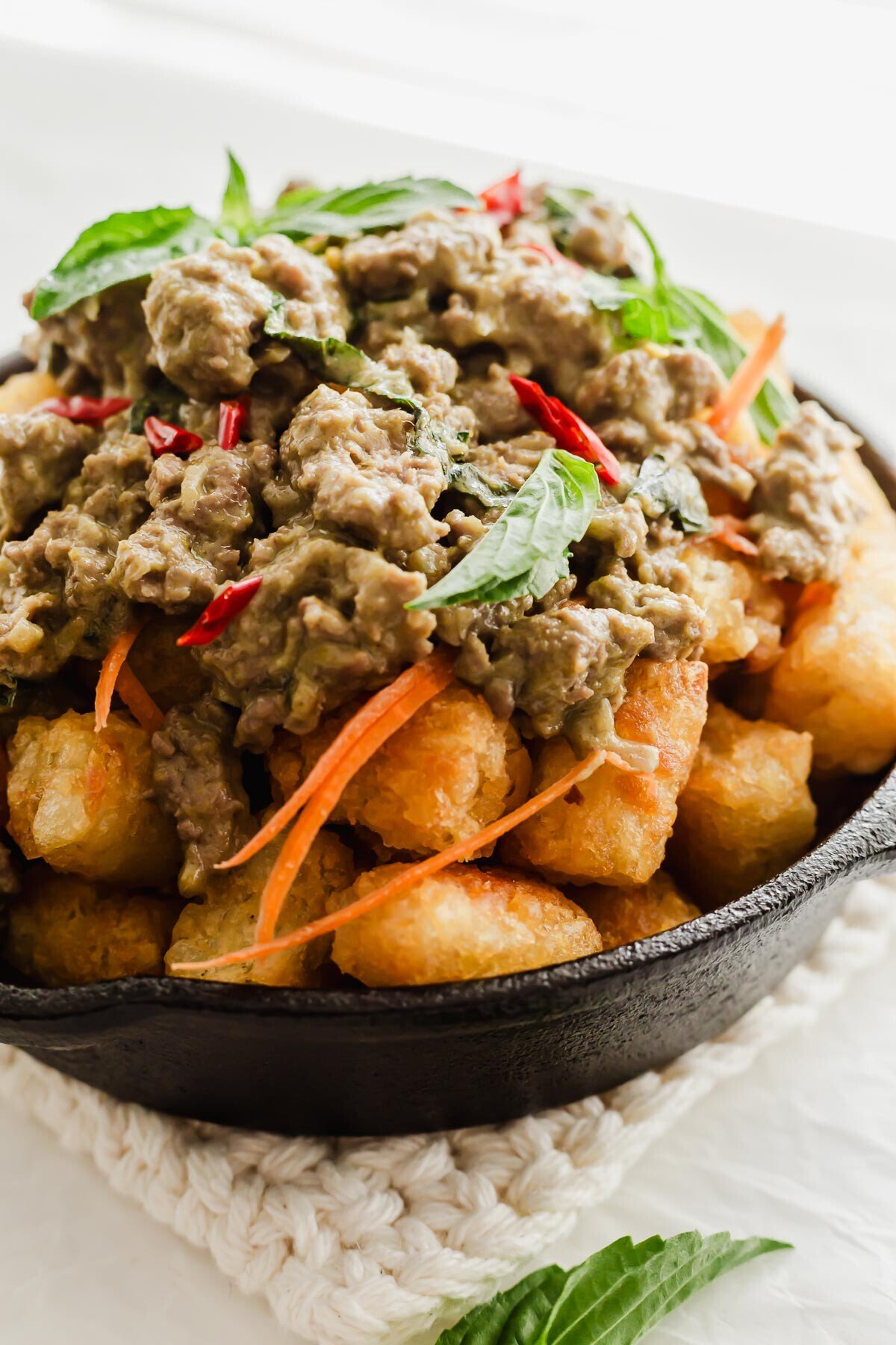 Thai green curry chicken on a bed of tater tots in skillet.