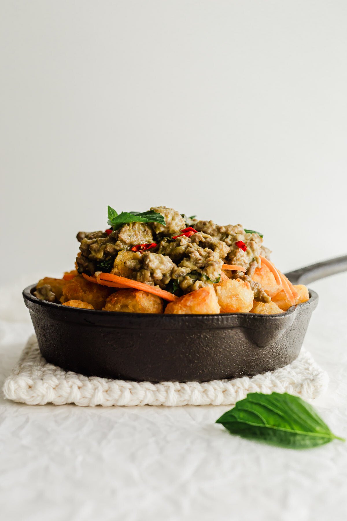 Thai green curry chicken on a bed of tater tots in skillet.