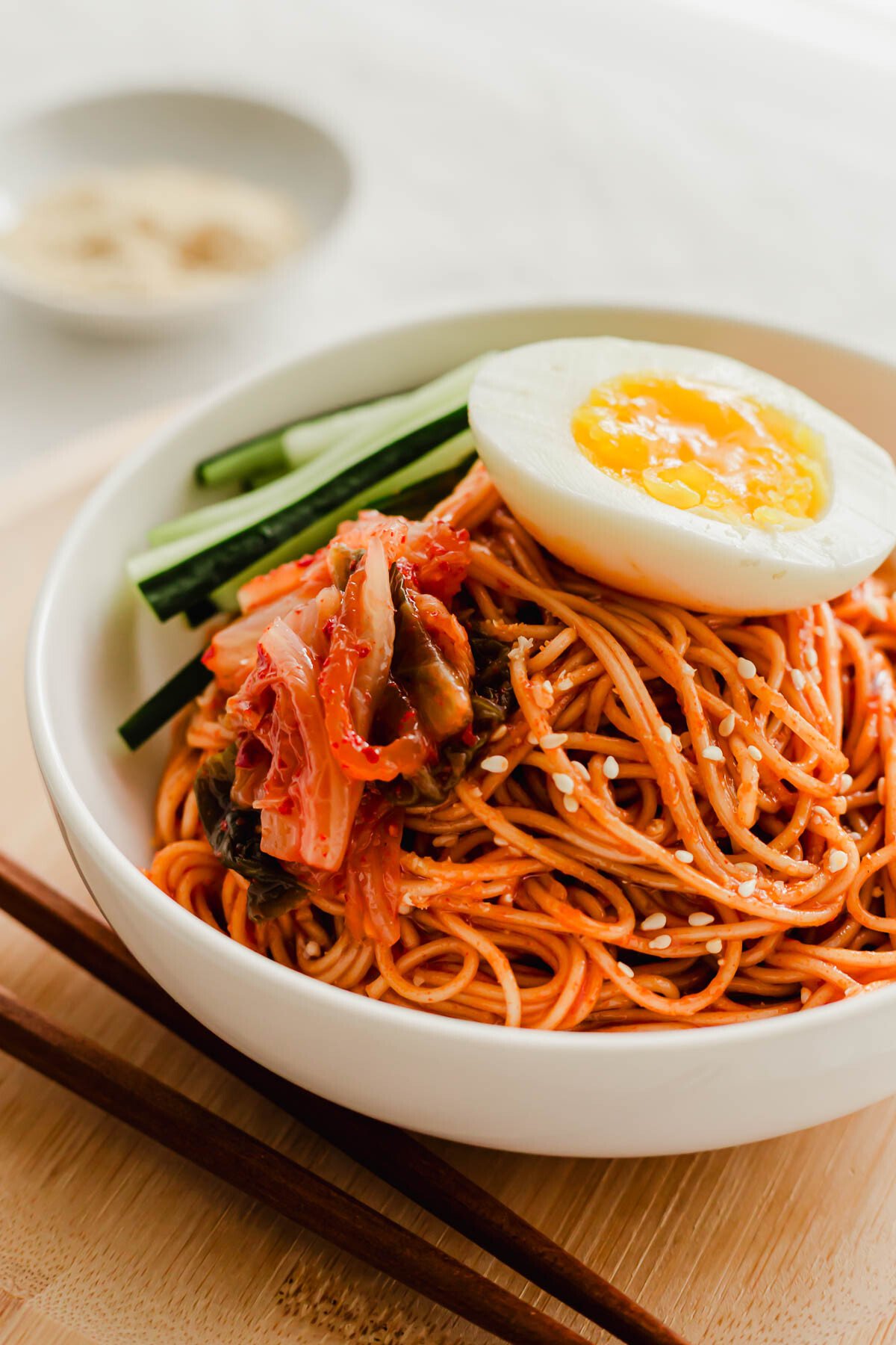 Korean bibim guksu noodles in a white bowl, topped with egg.