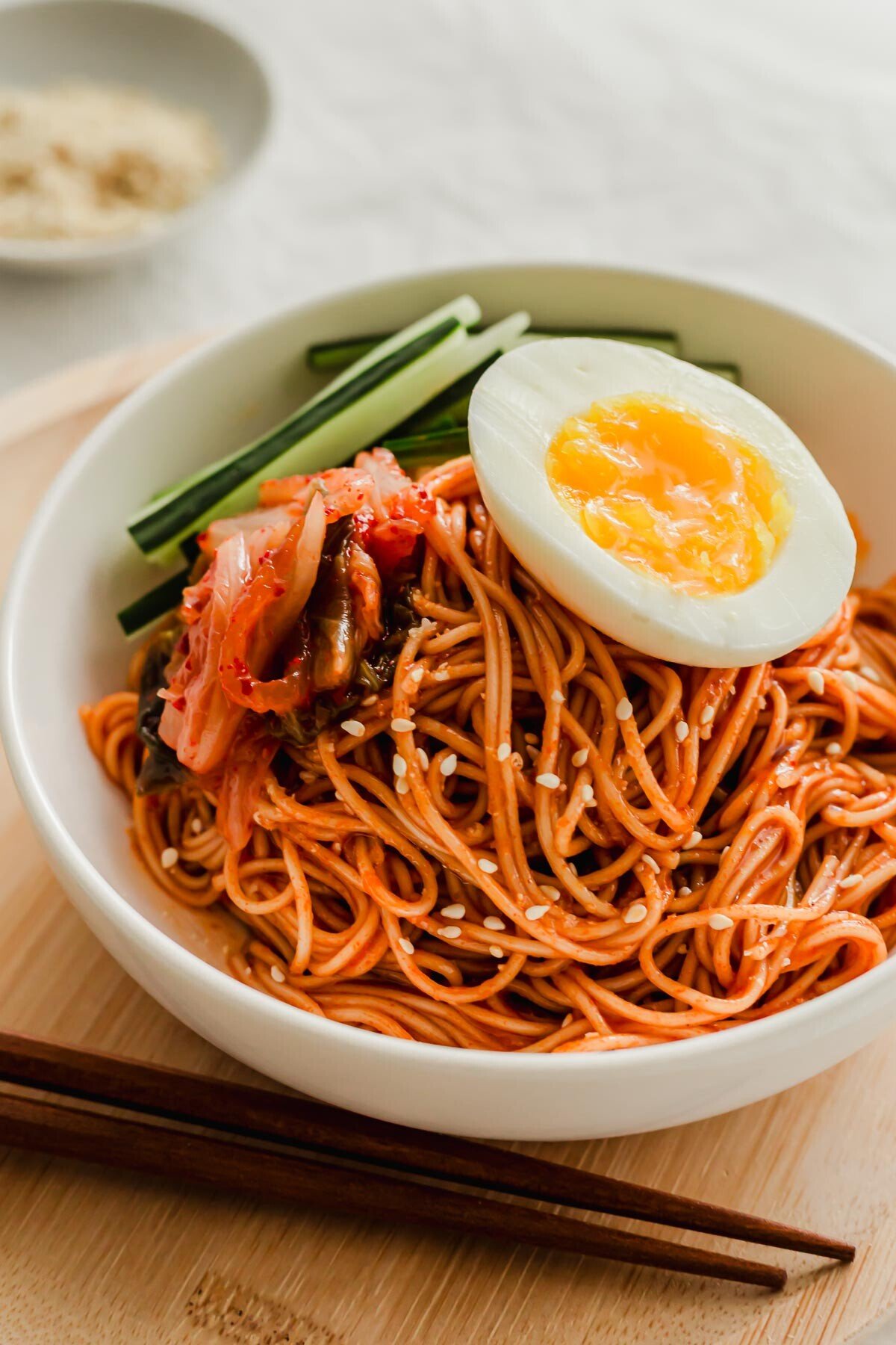 Korean bibim guksu noodles in a white bowl, topped with egg.