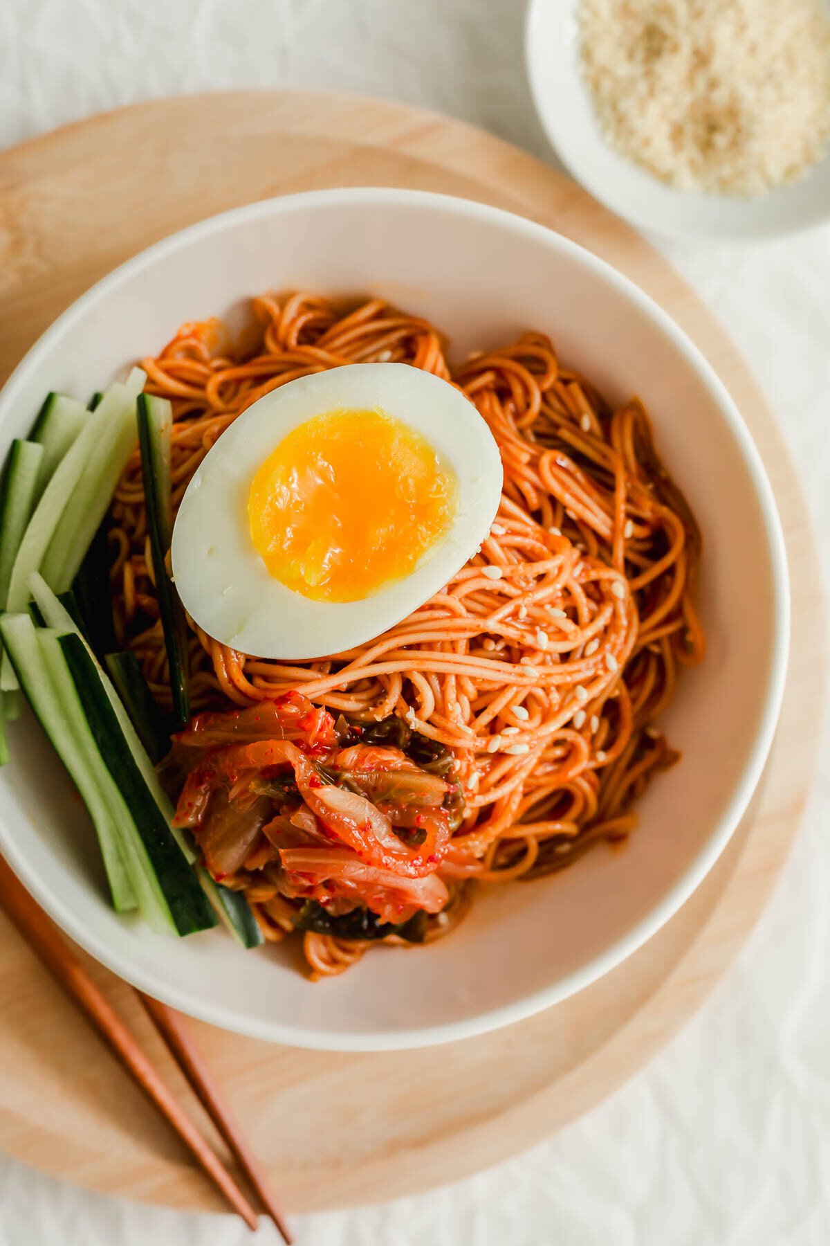Korean bibim guksu noodles in a white bowl, topped with egg.