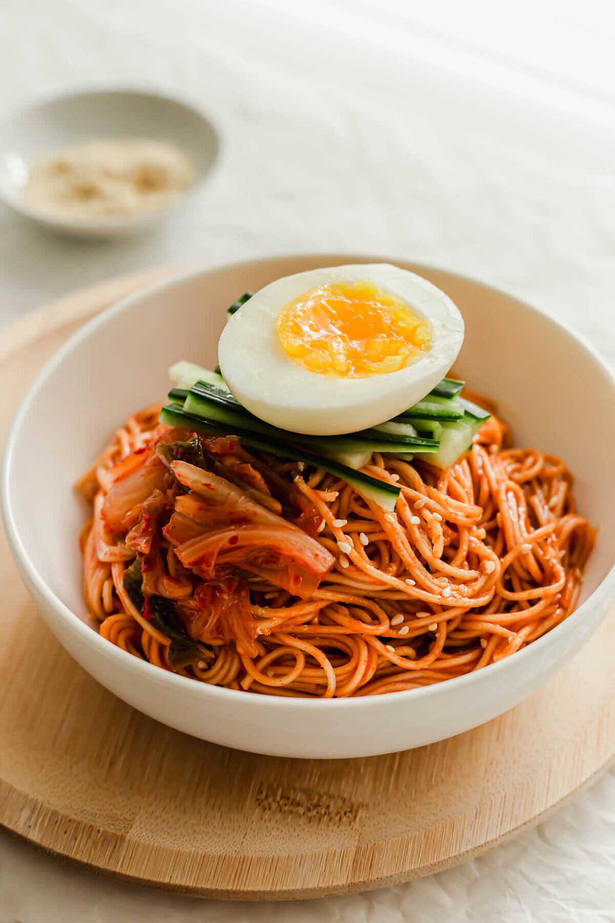 Korean bibim guksu noodles in a white bowl, topped with egg.