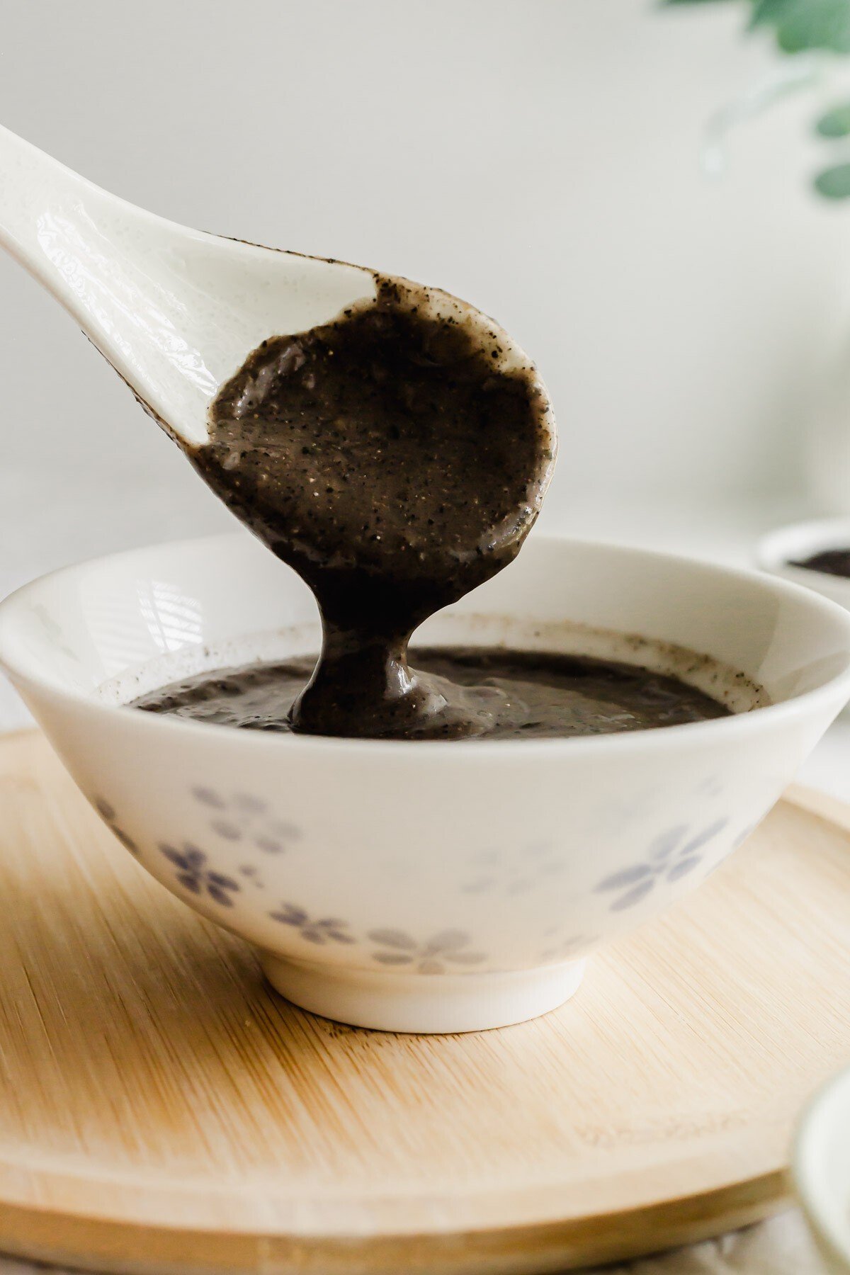 Black sesame soup dropping from a white spoon into a white bowl.