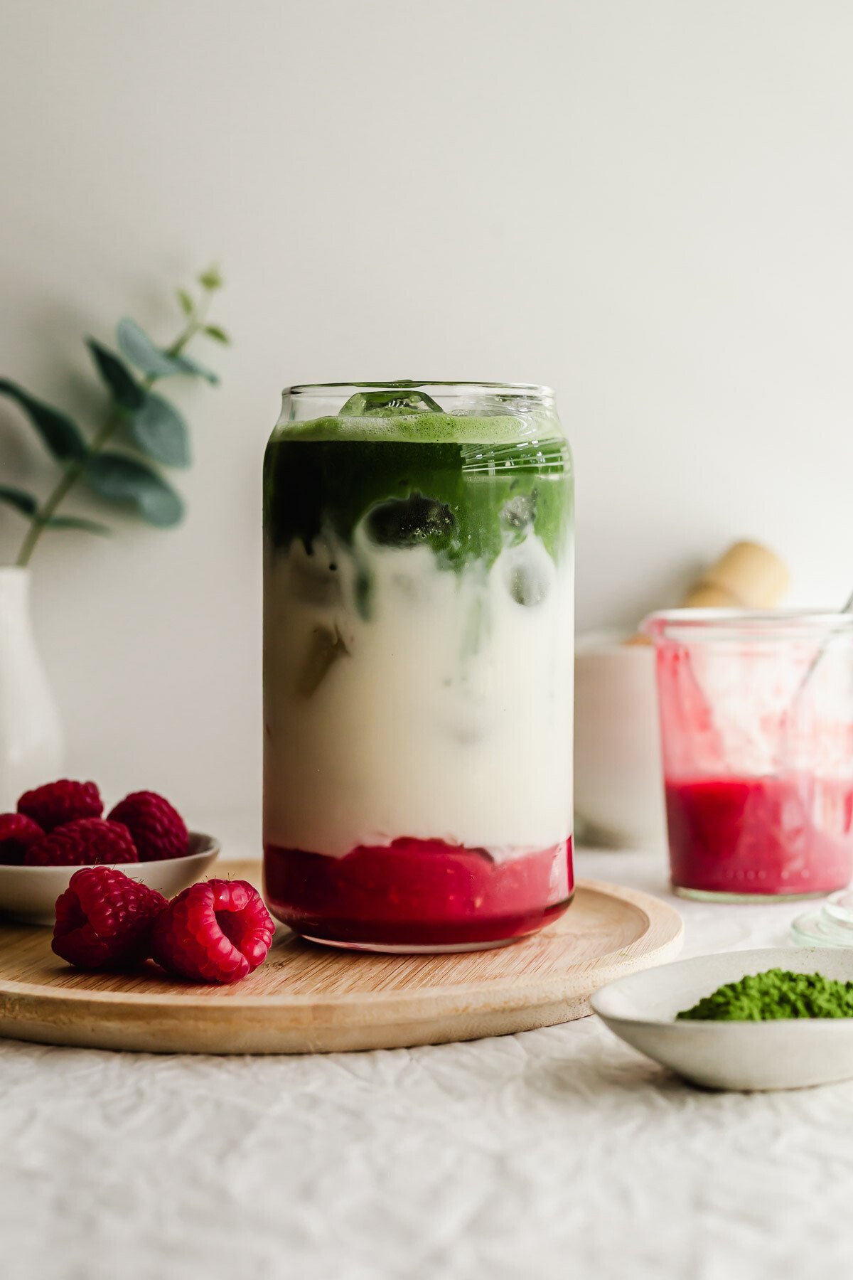 Raspberry matcha latte in a glass on wooden plate.