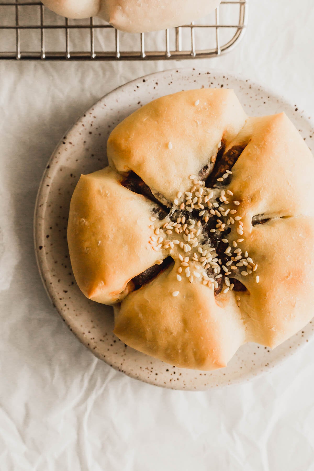 Baked flower shaped red bean bun on a speckled plate.