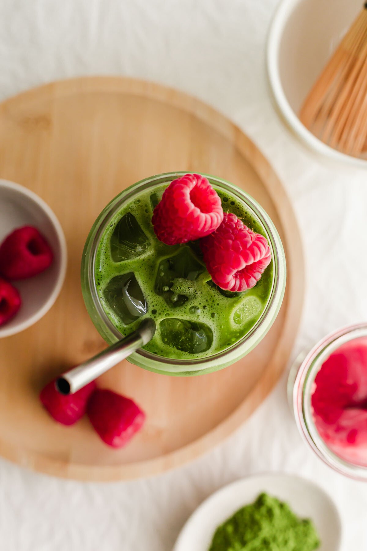 Raspberry matcha latte in a glass with straw and fresh raspberries on top.