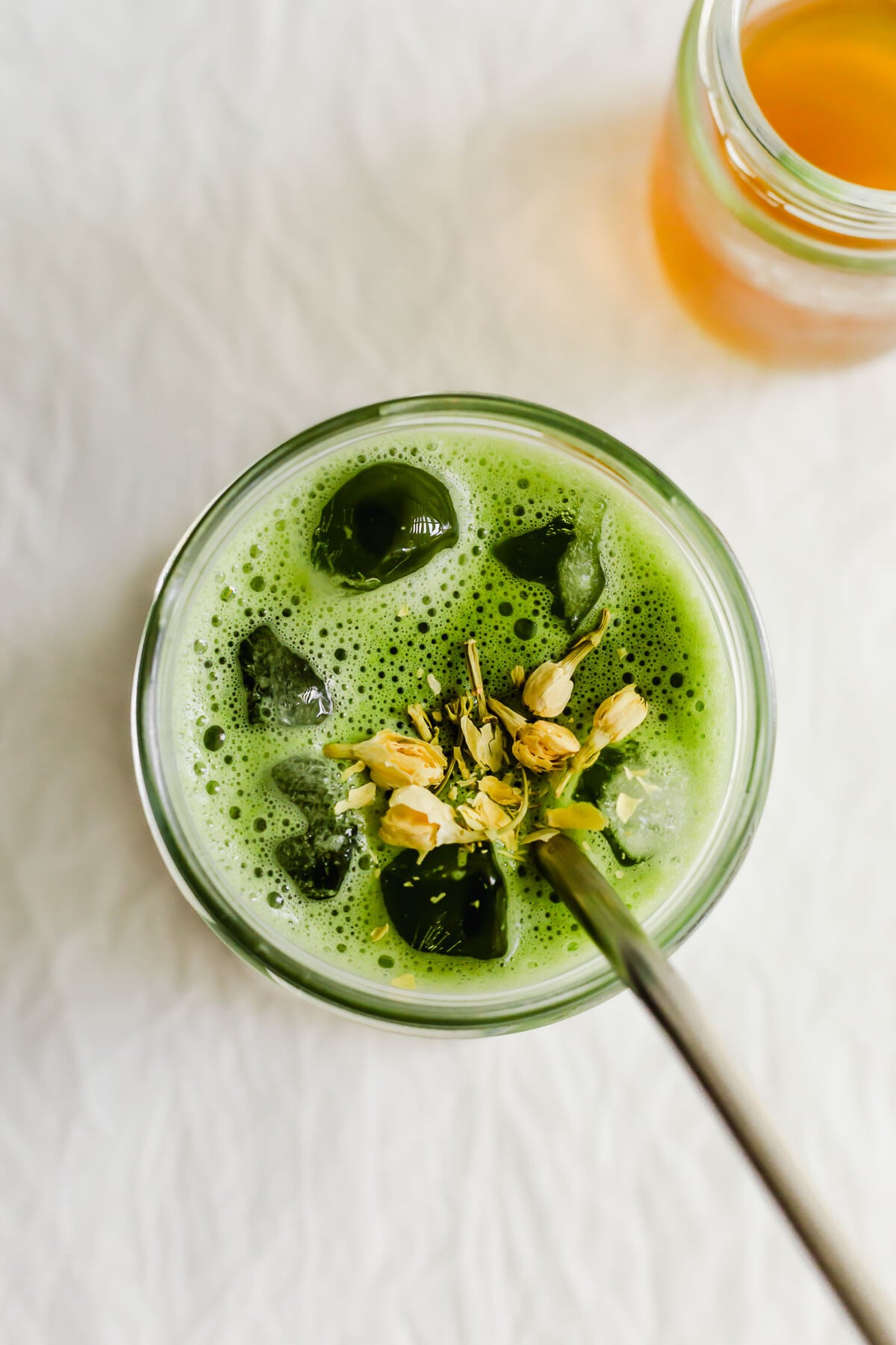 An overhead shot of matcha with jasmine flowers and a straw.