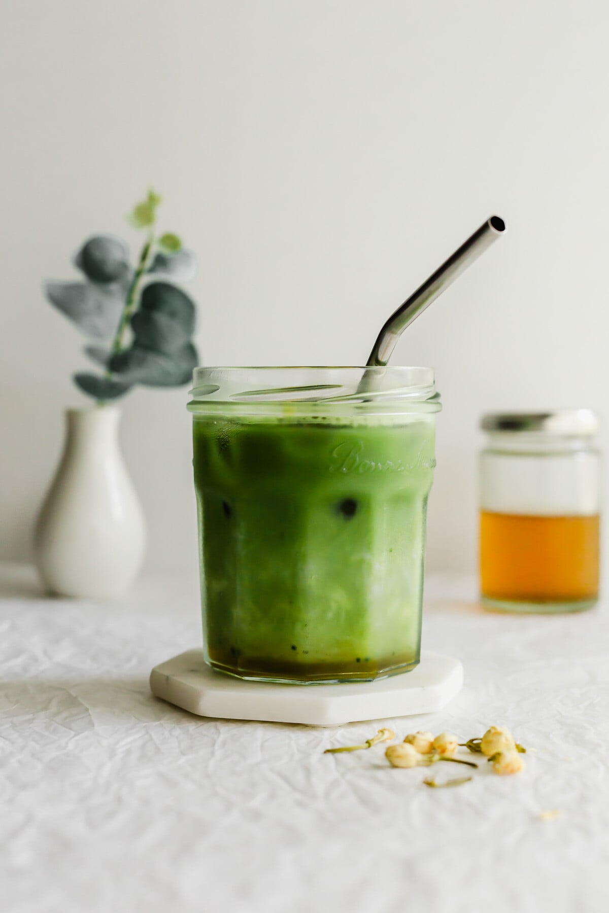 A glass of stirred jasmine matcha latte with straw.