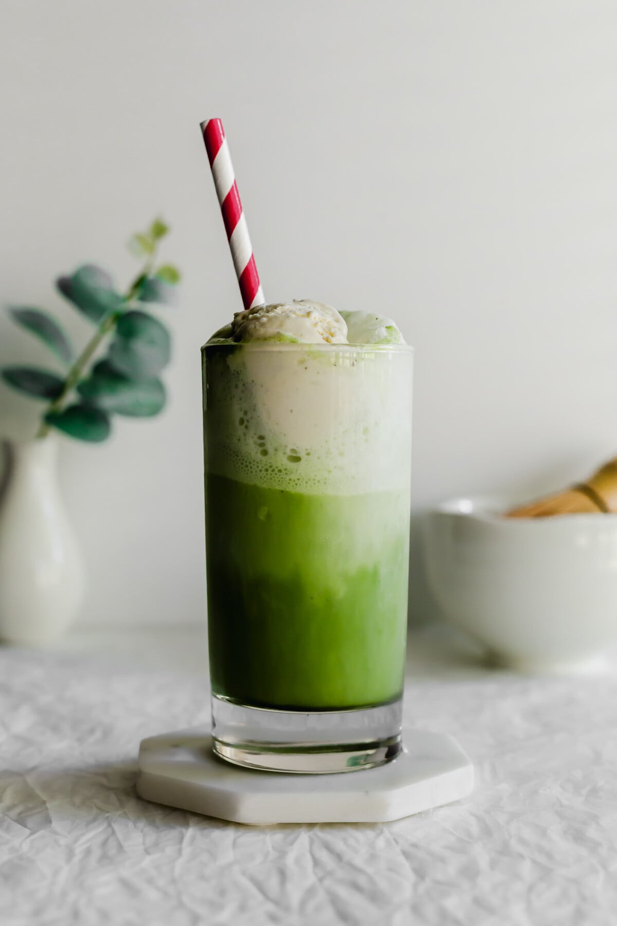 Matcha ice cream float in a glass with red and white straw.