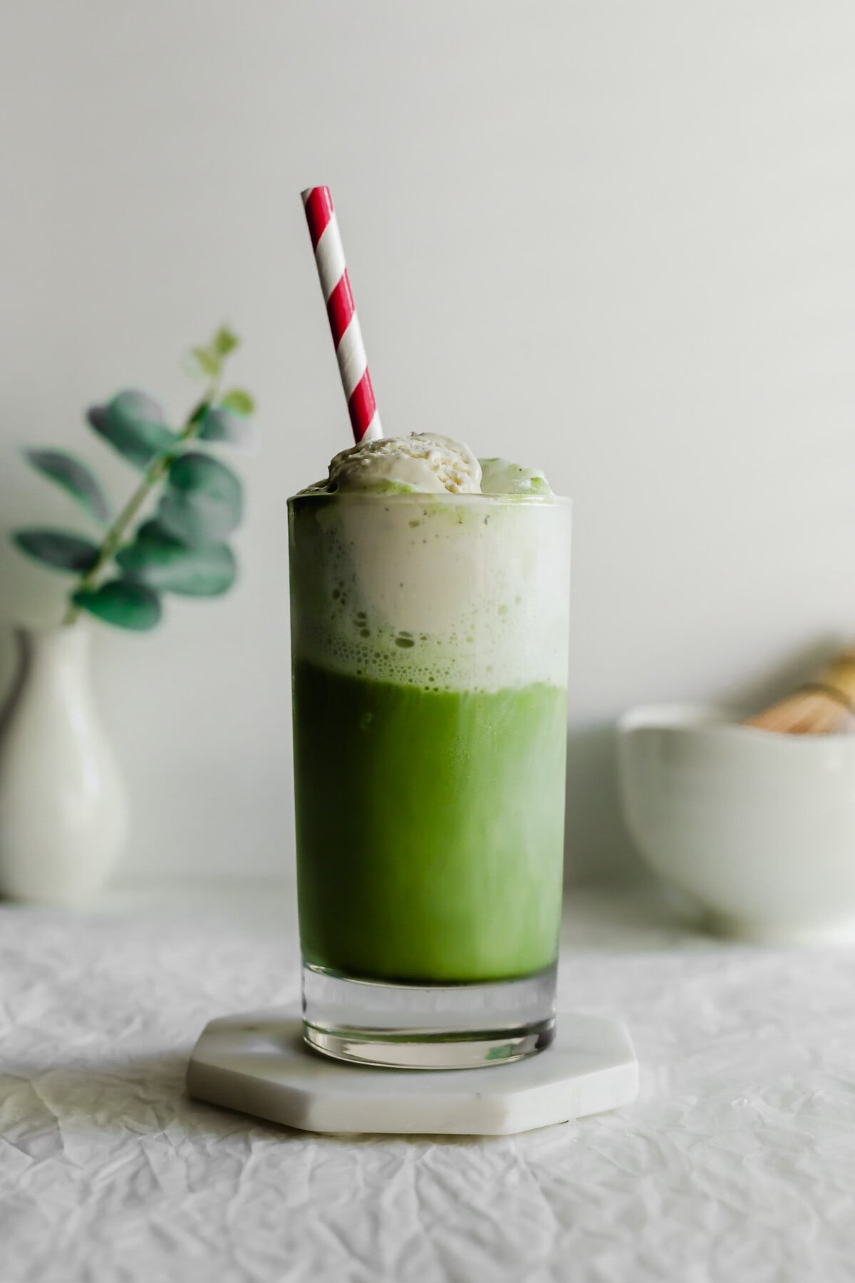 Matcha ice cream float in a glass with red and white straw.