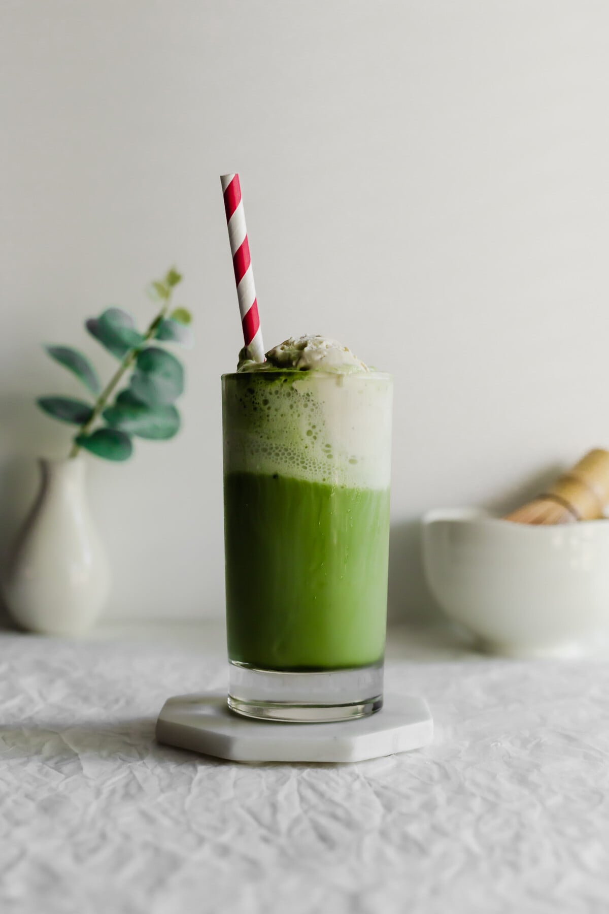 Matcha ice cream float in a glass with red and white straw.