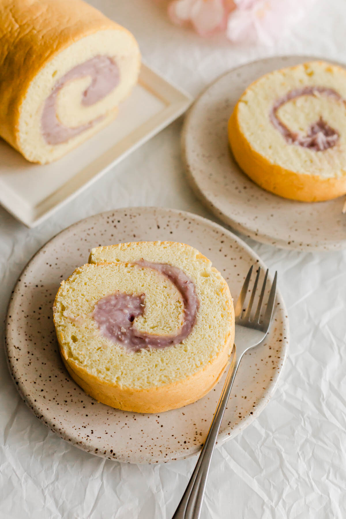 Slices of taro roll cake on speckled plates, with fork.