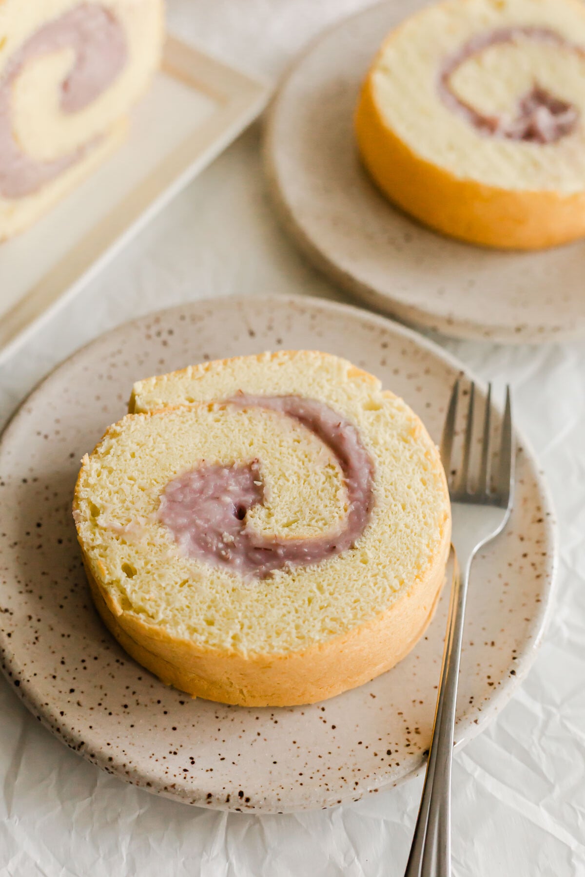 Close up of taro roll cake on a speckled plate, with fork.