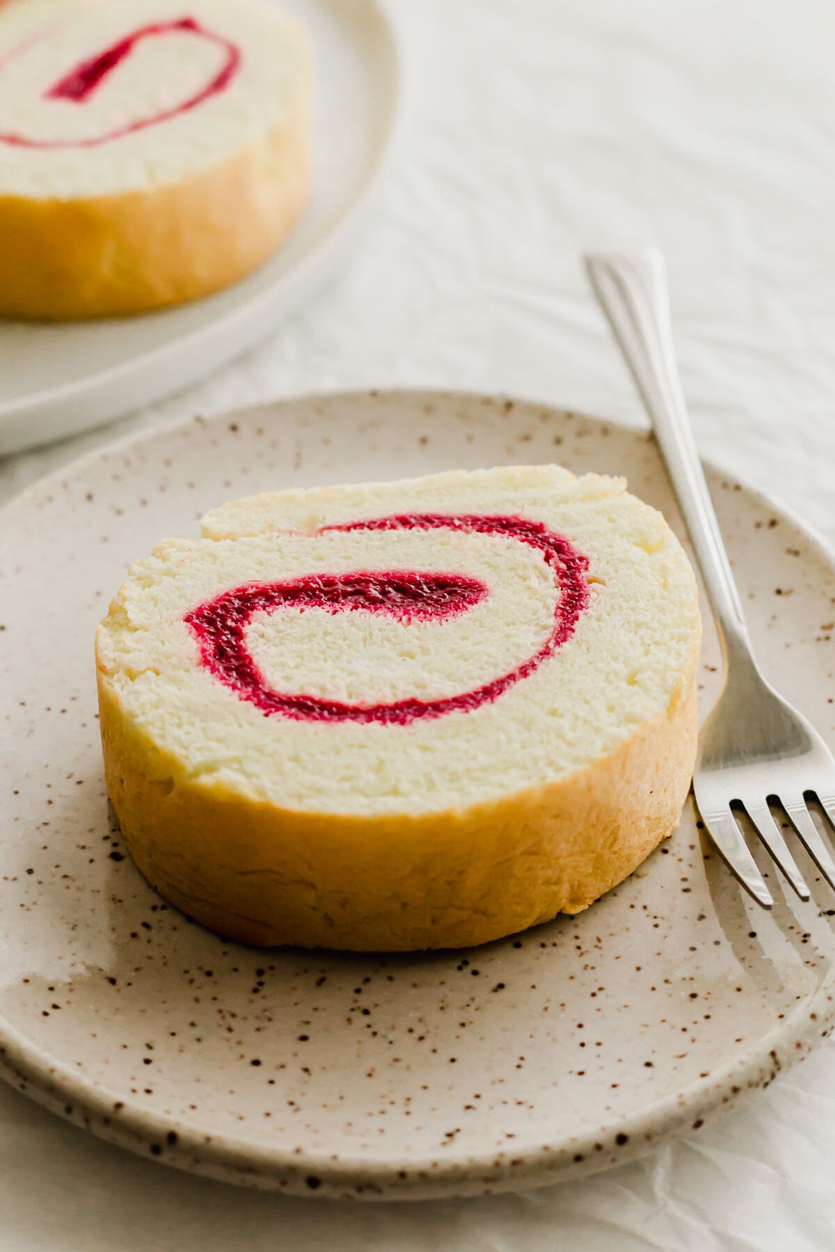 Slice of jelly Swiss roll cake on a speckled plate.