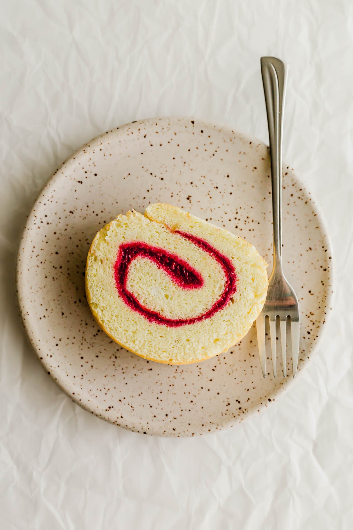 Slice of jelly roll cake on a speckled plate with fork.