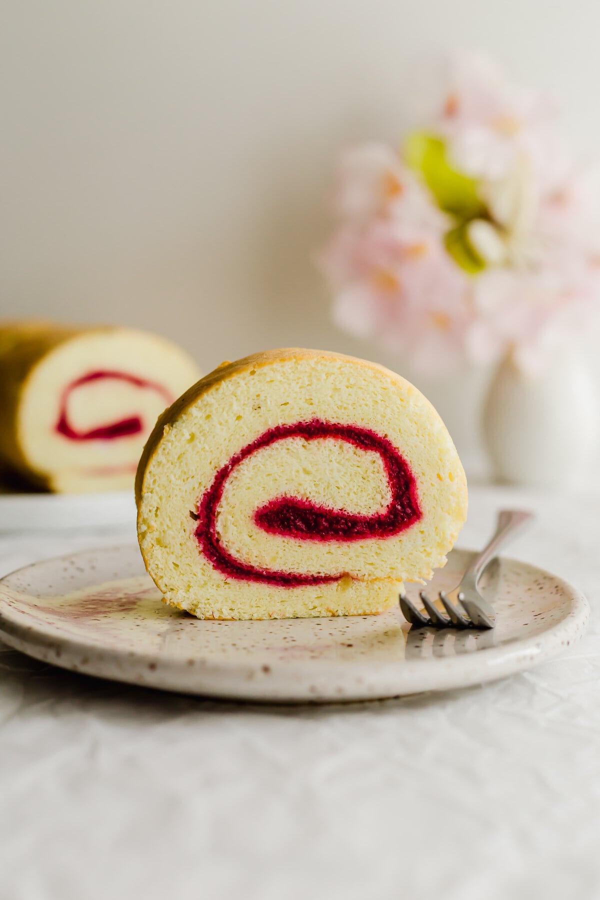Slice of jelly Swiss roll cake on a speckled plate.