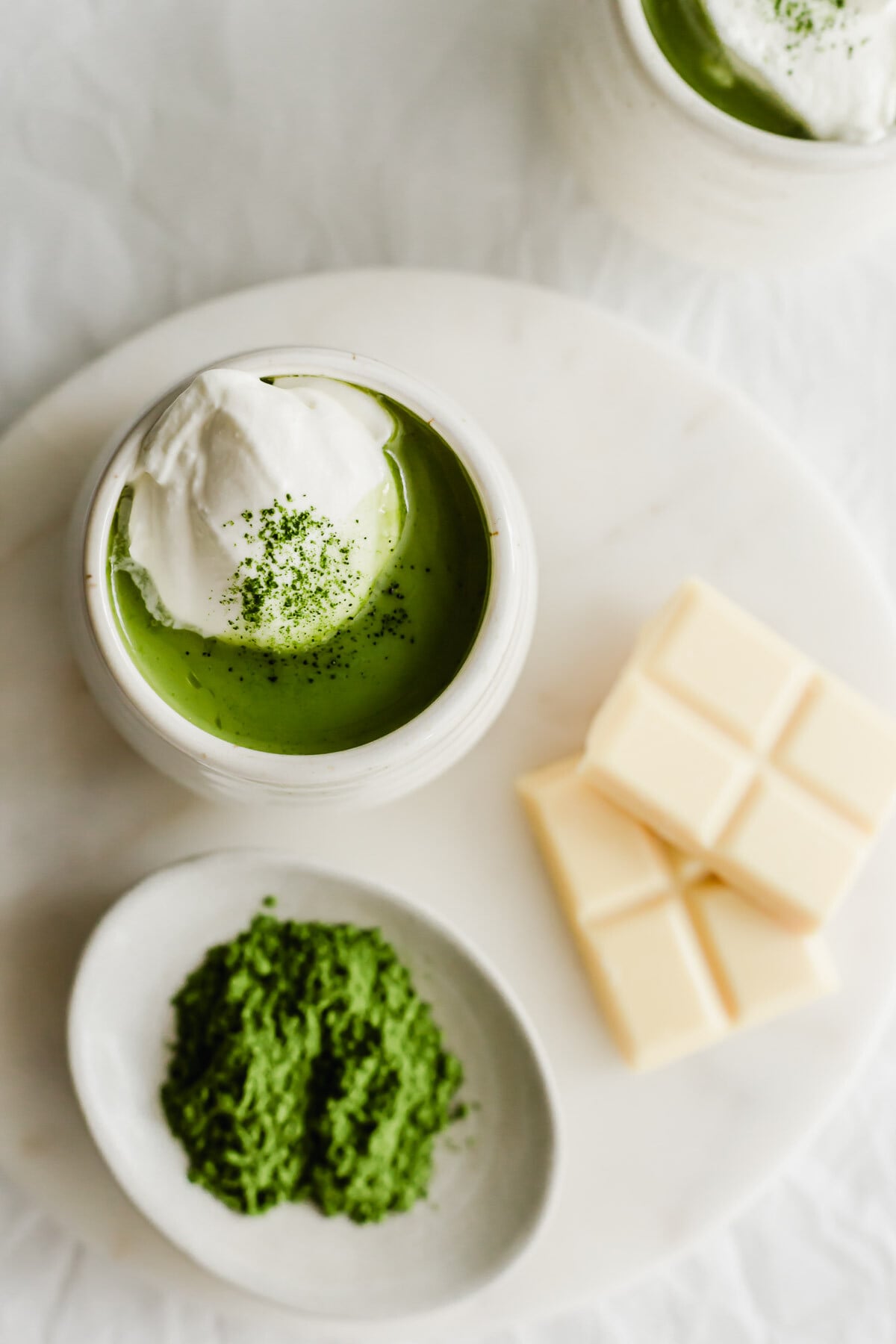 A mug of matcha hot chocolate on a white round marble.