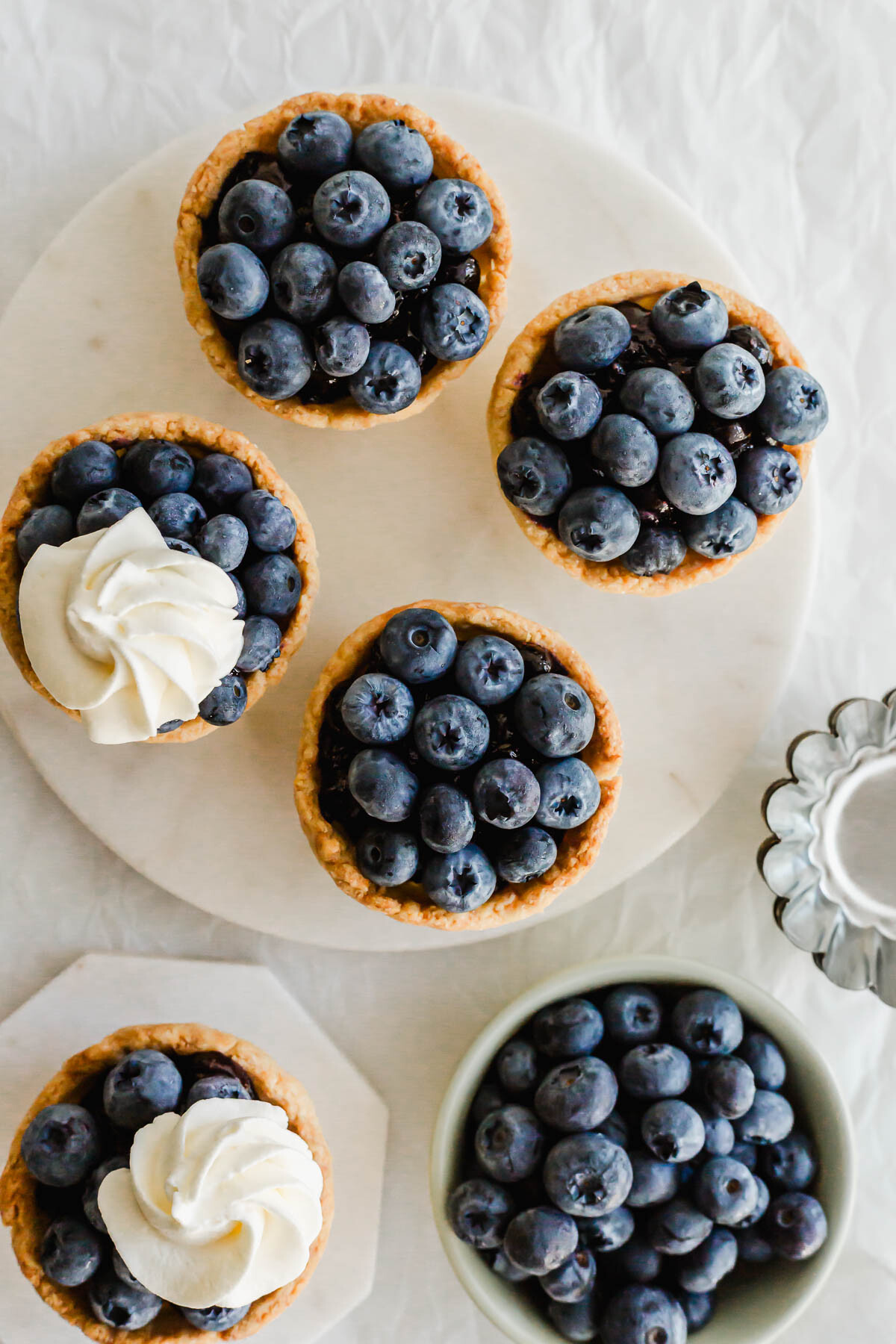 Mini blueberry tarts on a white round marble.