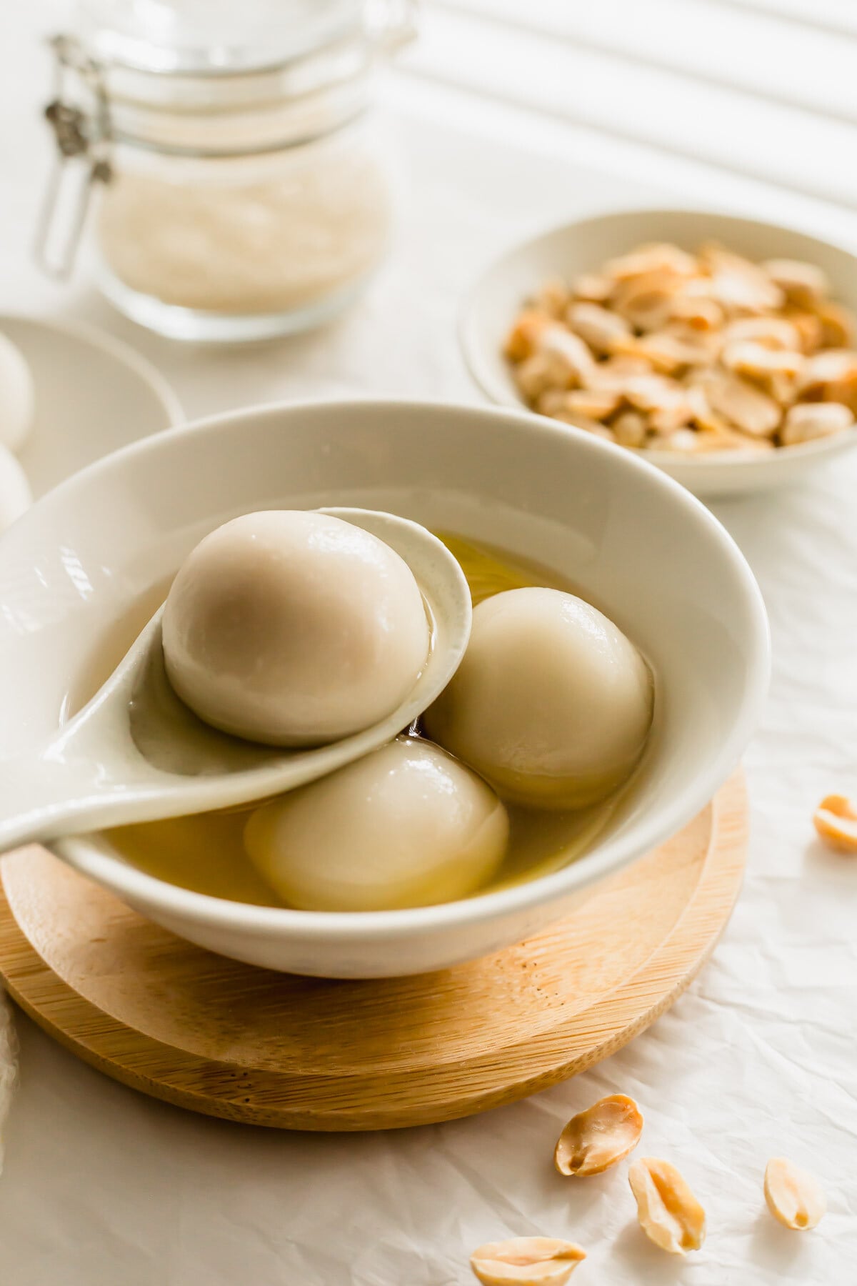 Peanut tang yuan in a white spoon resting on tang yuan in a bowl.