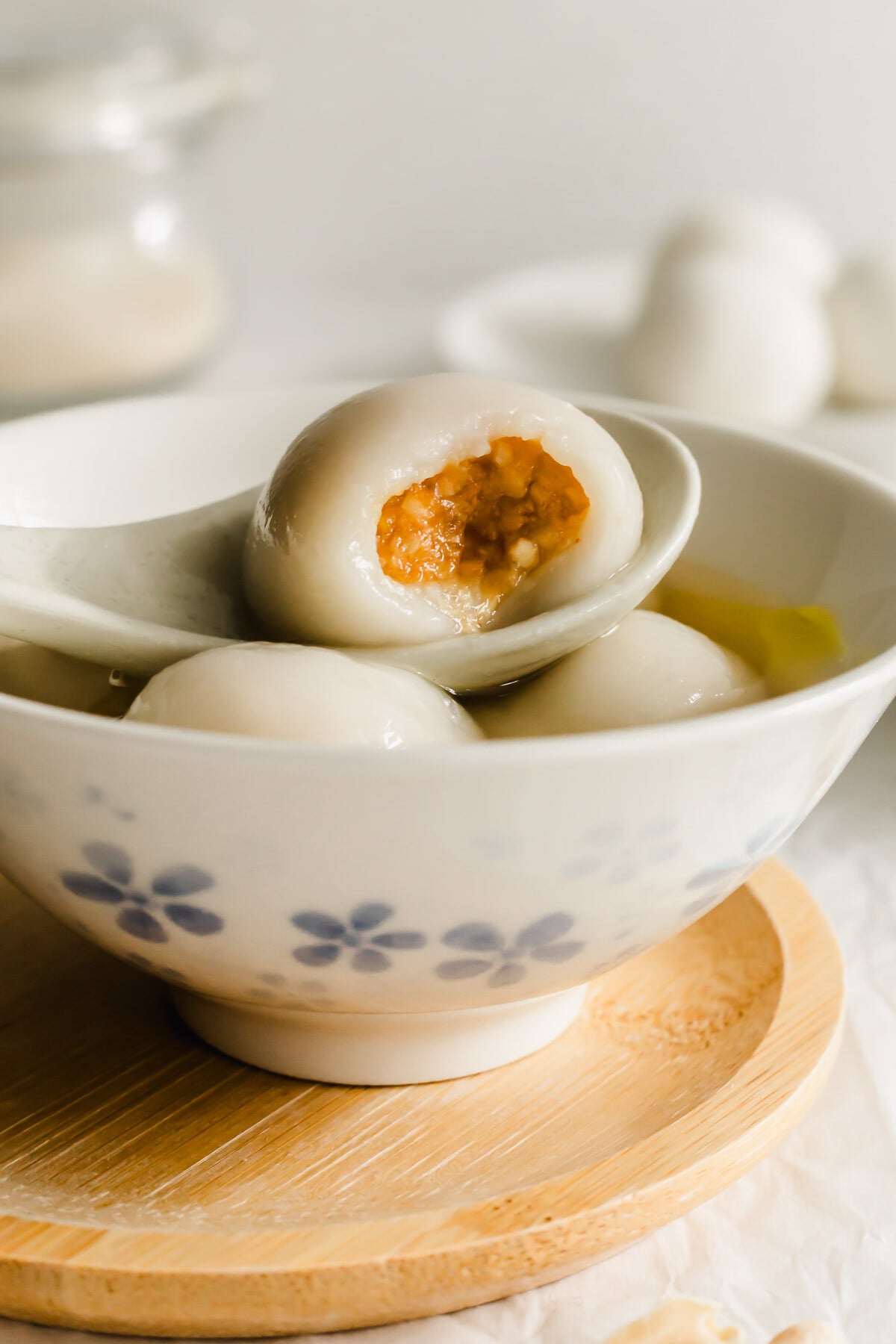 Close up of bitten peanut tang yuan resting on a spoon in a bowl with tang yuan dumplings.