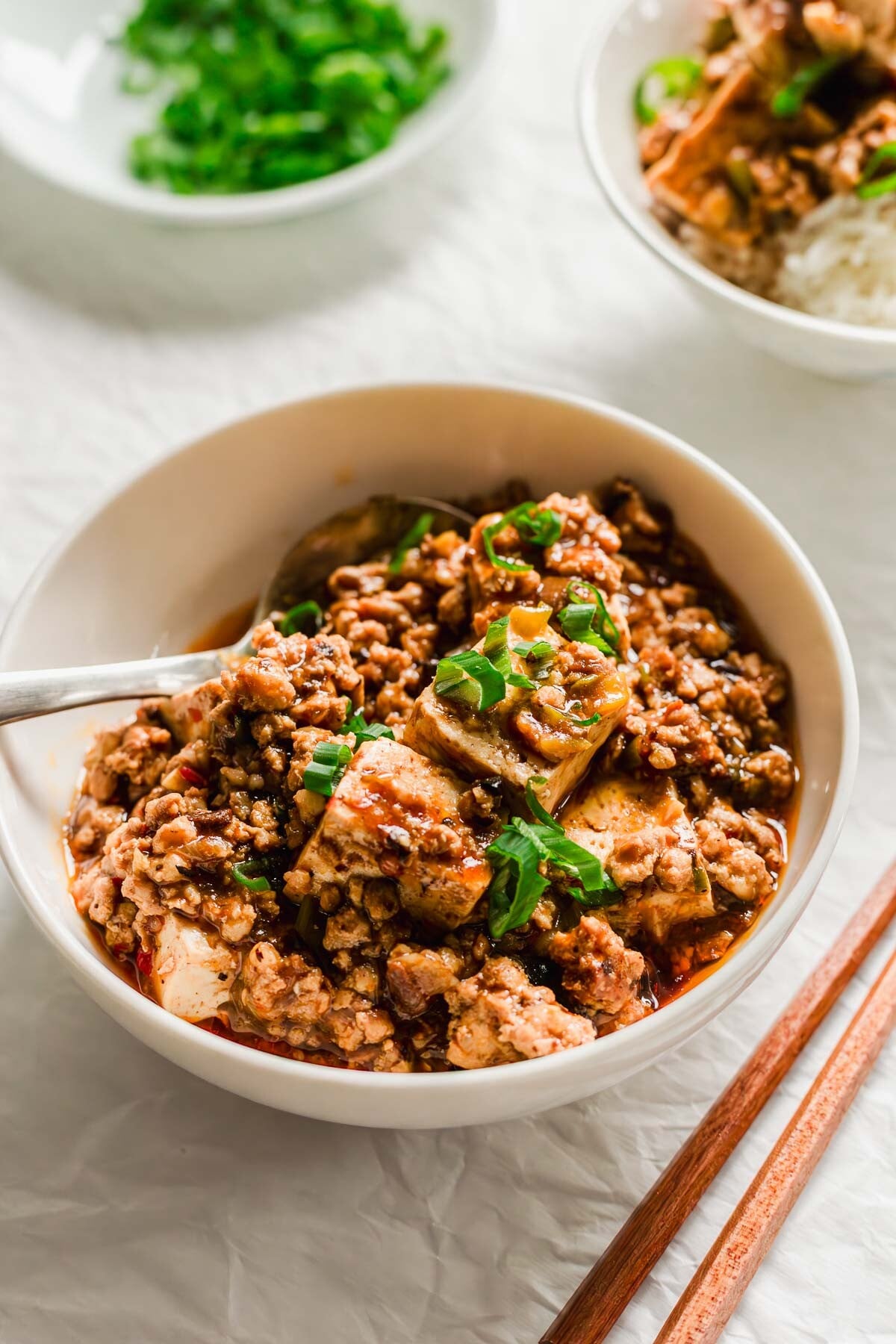 Chinese mapo tofu in a white bowl with ladle.