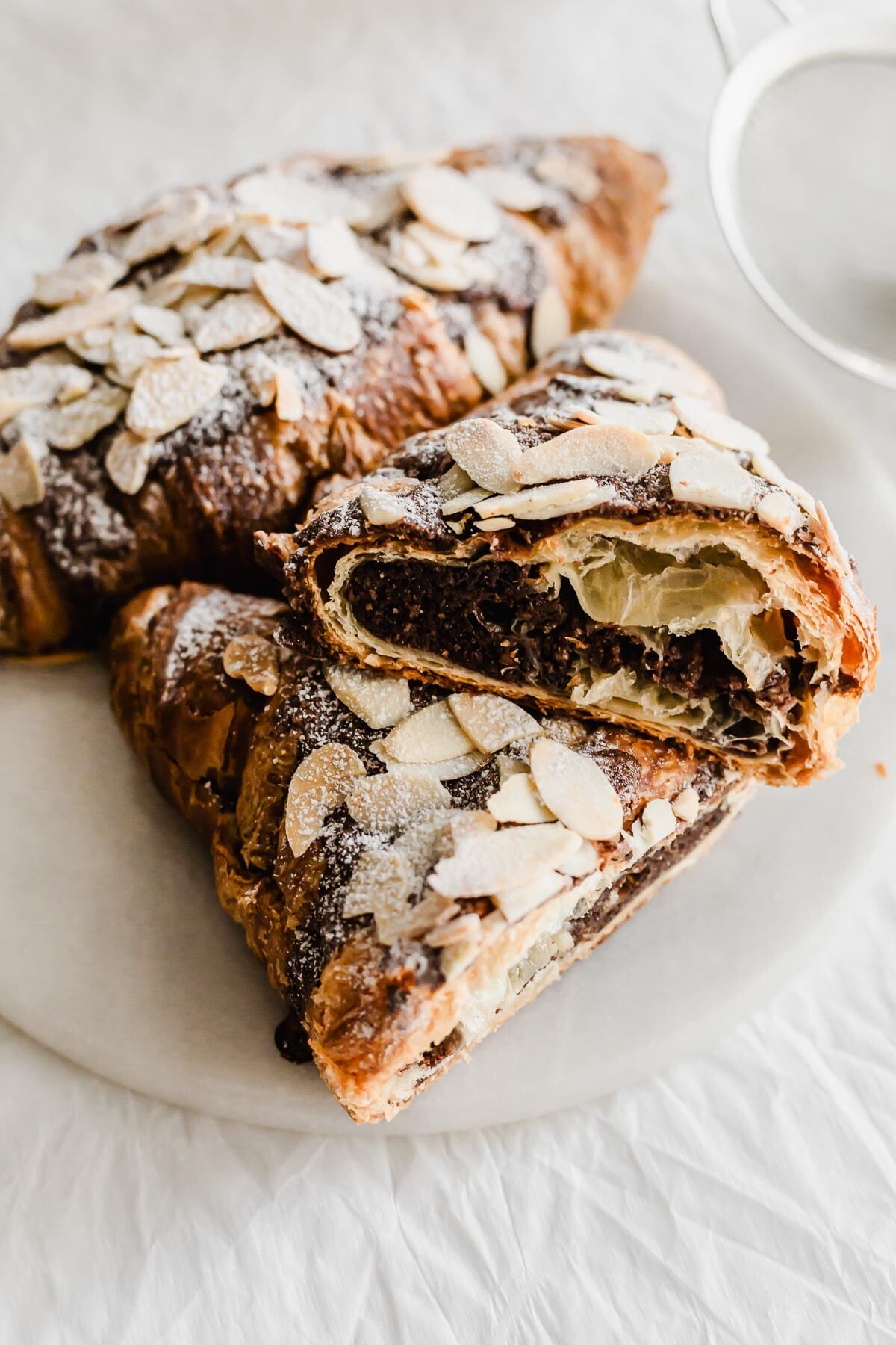 Cut open chocolate almond croissants stacked on a marble round.