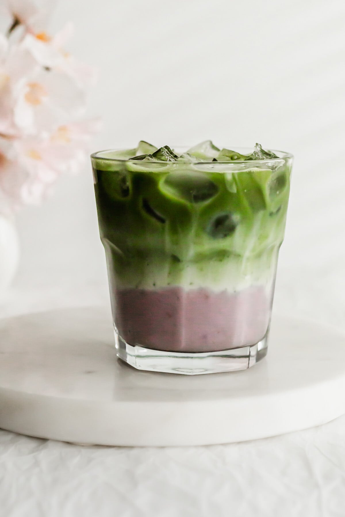 Matcha taro latte in a glass on white round marble.