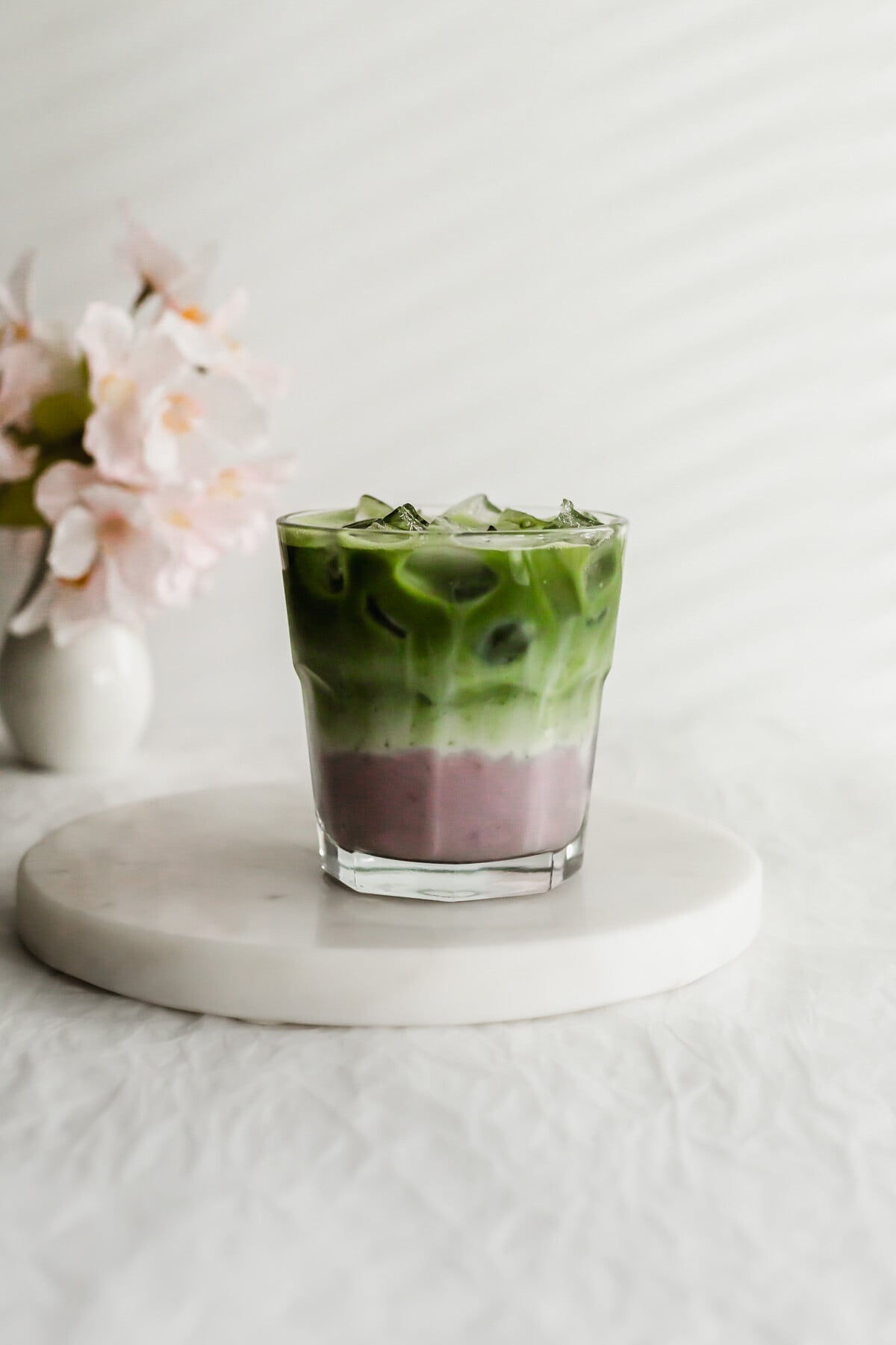 Matcha taro latte in a glass on white round marble.