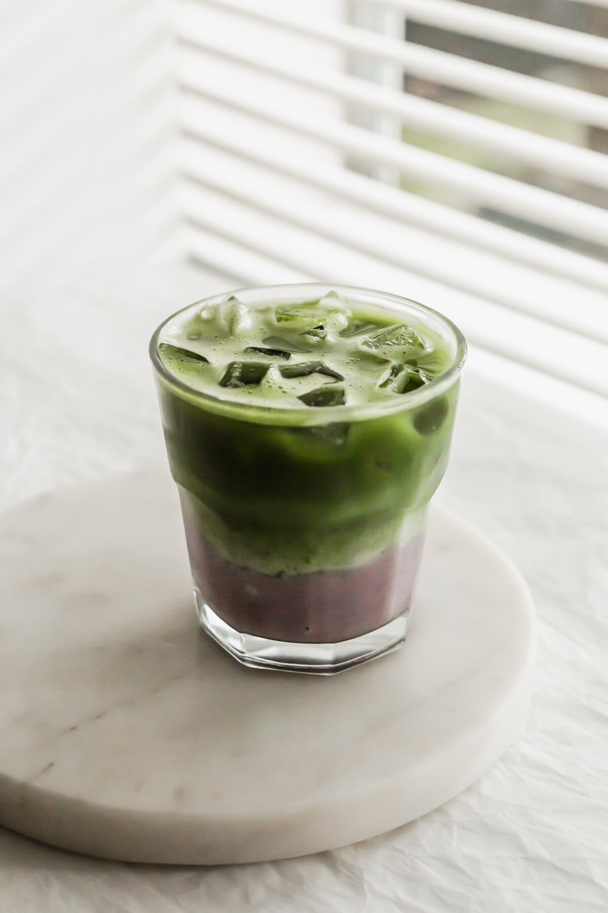 Matcha taro latte in a glass on white round marble.